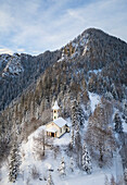 Luftaufnahme der Silvestri-Kirche und des Monte Scanapà während eines winterlichen Sonnenaufgangs. Presolana-Pass, Angolo Terme, Seriana-Tal, Provinz Brescia, Lombardei, Italien.