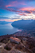 Luftaufnahme der kleinen Kirche San Defendente, die den Iseosee bei Sonnenuntergang dominiert. Solto Collina, Iseosee, Bezirk Bergamo, Lombardei, Italien.