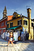 Burano, typischer Handwerkerladen mit Touristen und Blick auf den schiefen Glockenturm; Burano, Veneto, Italia, Italien, Europa, Südeuropa