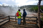 Couple look at Echinus acidic geyser in Yellowstone National Park, USA