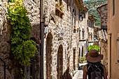 Woman wearing a straw hat, small street in the village classed as one of the most beautiful villages of france, saint-guilhem-le-desert, herault, occitanie, france