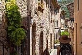 Frau mit Strohhut, kleine Straße in einem der schönsten Dörfer Frankreichs, saint-guilhem-le-desert, herault, okzitanien, frankreich