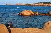 Paar mit Blick auf die rosa Granitfelsen des Leuchtturms von Ploumanach bei Sonnenuntergang, Renote Island Point, Tregastel, rosa Granitküste, Cotes-d'Armor, Bretagne, Frankreich