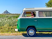 Woman at the steering wheel for a drive in the countryside in a volkswagen combi, mont-saint-michel, manche, normandy, france