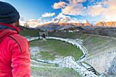 Mann bewundert den Sonnenuntergang vom Amphitheater der römischen Ausgrabungsstätte von Alba Fucens mit dem majestätischen Apennin des Regionalparks Sirente Velino, Bezirk Marsica, Provinz L'Aquila, Abruzzen, Italien