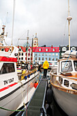 Tourist vor historischem Gebäude steht auf dem Pier zwischen Booten im Hafen von Torshavn, Streymoy Insel, Färöer Inseln, Dänemark, Europa