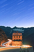 Sternspur auf dem berühmten Hotel Belvedere, beleuchtet von Autoscheinwerfern entlang der Furkapassstraße, Kanton Wallis, Schweiz