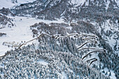 Aerial view of Maloja Pass mountain road crossing the snow capped forest, canton of Graubunden, Switzerland