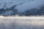 Fog over Lake Sils surrounding the village of Sils Maria covered with snow, canton of Graubunden, Engadin, Switzerland