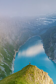 Aerial view of hiker man on rocks looking at lake Limmernsee in the mist at sunset, Canton of Glarus, Switzerland