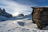Traditionelle, schneebedeckte Almhütte im Licht des Sonnenuntergangs, Grödnerjoch, Dolomiten, Südtirol, Italien