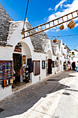 Tourists looking at souvenirs and Trulli huts in the old alley of Alberobello, province of Bari, Apulia, Italy