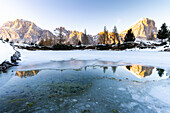 Sonnenaufgang über dem Lagazuoi und der Tofana di Rozes, die sich im teilweise zugefrorenen Limides-See spiegeln, Ampezzaner Dolomiten, Venetien, Italien