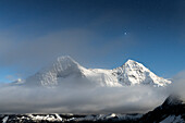 Starry sky over the snowcapped Eiger and Monch mountains covered by fog at night, Mannlichen, Bern canton, Switzerland