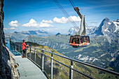Eine Person schaut vom gläsernen Panoramagang Thrill Walk auf die Seilbahn, Murren Birg, Jungfrau, Kanton Bern, Schweiz