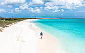 Fröhlicher Tourist mit hawaiianischem Hemd, der an einem weißen Sandstrand am kristallklaren Karibischen Meer spazieren geht, Antigua & Barbuda, Westindische Inseln