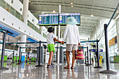 Cute little boy and mother holding hands while checking the schedule of flight at the departure area of airport