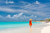 Frau mit Sonnenhut spaziert über einen weißen Sandstrand, der von Wellen umspült wird, Barbuda, Antigua & Barbuda, Karibik, Westindien