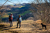 Two women with backpack and dog admiring the apennines. Modigliana, Forlì, Emilia Romagna, Italy, Europe.