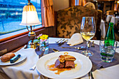 Beef tenderloin and foie dish. Interior of restaurant car railway carriage of Transcantabrico Gran Lujo luxury train travellong across northern Spain, Europe. First Class dining area railway coach.