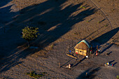 An aerial view of a traditional house with a thatched roof. People working in the yard. Maun, Okavango Delta, Botswana.