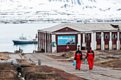 Männer in arktischer Schutzkleidung gehen auf ein verankertes Schiff zu. Barentsburg, Insel Spitzbergen, Svalbard, Norwegen.