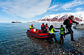 Tourists disembark from an inflatable raft onto Bockfjorden's shore. Bockfjorden, Spitsbergen Island, Svalbard, Norway.