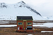 Ein bunt bemaltes Gebäude und Berge an der Forschungsstation, Ny-Alesund. Ny-Alesund, Kongsfjorden, Insel Spitzbergen, Svalbard, Norwegen.