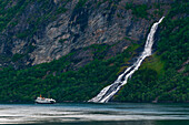 Ein Kreuzfahrtschiff in der Nähe von Wasserfällen im Geirangerfjord. Geirangerfjord, Norwegen.