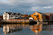 Hell gestrichene, sonnenbeschienene Häuser im Fischerdorf Svolvaer spiegeln sich im Wasser des Hafens. Svolvaer, Austvagoya-Insel, Lofoten, Norwegen.