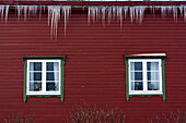Eiszapfen hängen an einem roten Haus mit grün umrahmten Fenstern. Noss, Vesteralen-Inseln, Nordland, Norwegen.