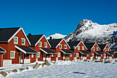 Eine Reihe roter Gebäude, die Svinoya Rorbuer Apartments, in einer verschneiten Landschaft. Svolvaer, Lofoten-Inseln, Nordland, Norwegen.