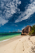 Wispy clouds over a sandy tropical beach with a large stone rock formation. Anse Source d'Argent Beach, La Digue Island, The Republic of the Seychelles.