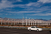 Ein Auto fährt an einem Windpark am San-Gorgonio-Pass in der Nähe von Palm Springs vorbei. San-Gorgonio-Pass, San-Jacinto-Berge, Riverside County, Kalifornien, USA.