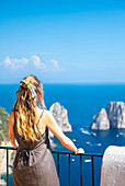 Ein blondes Mädchen bewundert die Faraglioni-Felsen. Insel Capri, Kampanien, Italien