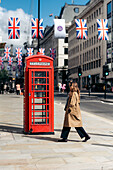 A blonde girl walking to a phone cabin in 2022 Jubilee dressed street of London, United Kingdom