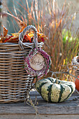 Ornamental pumpkin next to a wicker basket with autumn leaves and a wreath of broom heather (Calluna vulgaris)