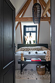 Doppelbett, davor schwarze Holzbank mit Dekoration und schwarze Hängelampe im Schlafzimmer