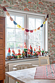 Garden gnome collection on a windowsill in the dining room with vintage wallpaper