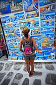 Young woman looking at paintings in street store, Mykonos, Greece