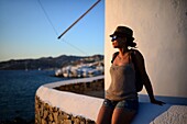 Junge Frau genießt den Sonnenuntergang vor traditionellen Windmühlen (Kato Milli) in Mykonos-Stadt, Griechenland