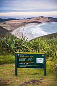 Schild des Te Paki Coastal Track, dahinter der Te Werahi Beach, Cape Reinga, Neuseeland