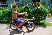Palmen und jugendliche Radfahrer an der Route de ceinture, Tahiti Nui, Gesellschaftsinseln, Französisch-Polynesien, Südpazifik.