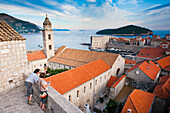 Touristen bei der Besichtigung der Stadtmauern von Dubrovnik, Altstadt von Dubrovnik, Dalmatien, Kroatien. Dies ist ein Foto von Touristen auf der Stadtmauer von Dubrovnik. Es zeigt das Dominikanerkloster in der zum UNESCO-Weltkulturerbe gehörenden Altstadt von Dubrovnik, mit der Insel Lokrum im Hintergrund. Für die meisten Touristen sind die Stadtmauern von Dubrovnik zweifellos der Höhepunkt eines Besuchs dieser schönen, historischen Stadt an der dalmatinischen Küste Kroatiens. Die Stadtmauern von Dubrovnik bieten einen unvergleichlichen Blick auf die Altstadt von Dubrovnik, die Insel Lokrum 