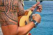 Local tattooed person playing the ukulele in Huahine, Society Islands, French Polynesia, South Pacific.