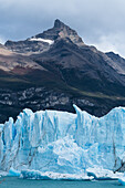 The jagged face of Perito Moreno Glacier and Lago Argentino in Los Glaciares National Park near El Calafate, Argentina. A UNESCO World Heritage Site in the Patagonia region of South America. Icebergs from calving ice from the glacier float in the lake. Behind is the peak of Cerro Moreno with waterfalls on its face.