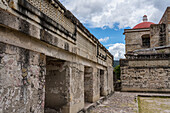 Laubsägearbeitstafeln aus Stein an den Wänden von Hof B (Viereck B) in den Ruinen der zapotekischen Stadt Mitla in der Nähe von Oaxaca, Mexiko. Dahinter befindet sich die Kirche von San Pablo. Ein UNESCO-Weltkulturerbe.