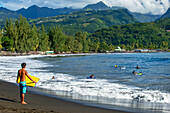 Surfer am Strand mit schwarzem Sand auf Pointe Venus, Tahiti, Französisch-Polynesien, Tahiti Nui, Gesellschaftsinseln, Französisch-Polynesien, Südpazifik.