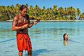 Insel Taha'a, Französisch-Polynesien. Ein einheimischer Junge spielt Ukulele, um Ihr Mädchen auf dem Motu Mahana zu umwerben, Taha'a, Gesellschaftsinseln, Französisch-Polynesien, Südpazifik.