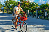Einheimisches Mädchen mit einem Fahrrad und einem kleinen Kind in Fakarava, Tuamotus-Archipel, Französisch-Polynesien, Tuamotu-Inseln, Südpazifik.